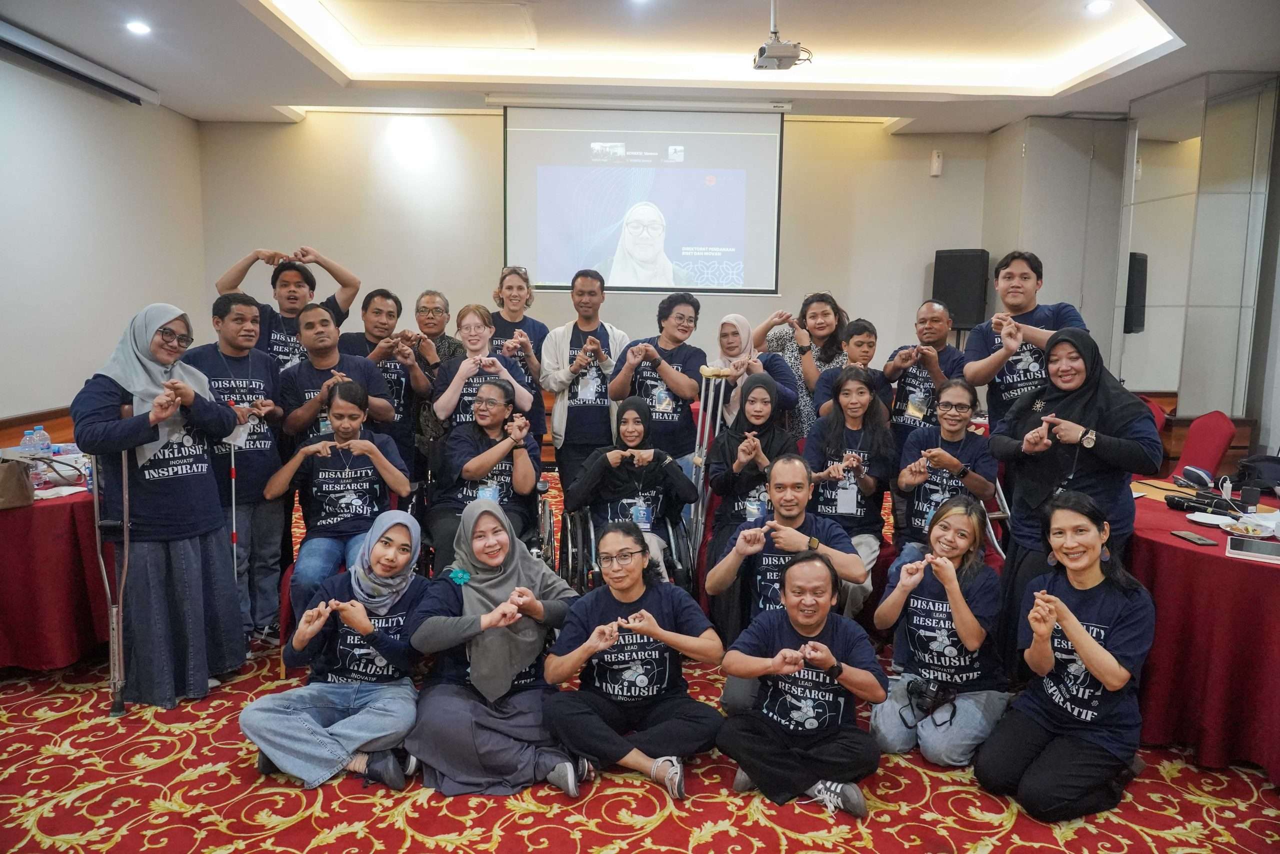 Gambar menunjukkan foto bersama seluruh peserta kelas intensif SAPDA, perwakilan KONEKSI, perwakilan BRIN, dan tim SAPDA menggunakan kaos biru bertuliskan Disability Lead Research
