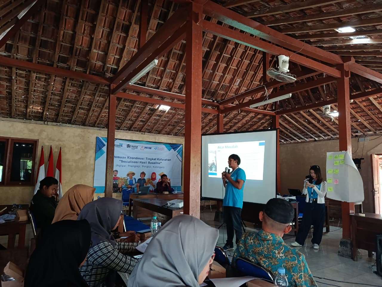 Gambar menunjukkan kondisi kegiatan konsorsium penguatan kapasitas di kalurahan nglipar. Nampak seorang laki-laki sedang melakukan presentasi di depan belasan orang di sebuah joglo