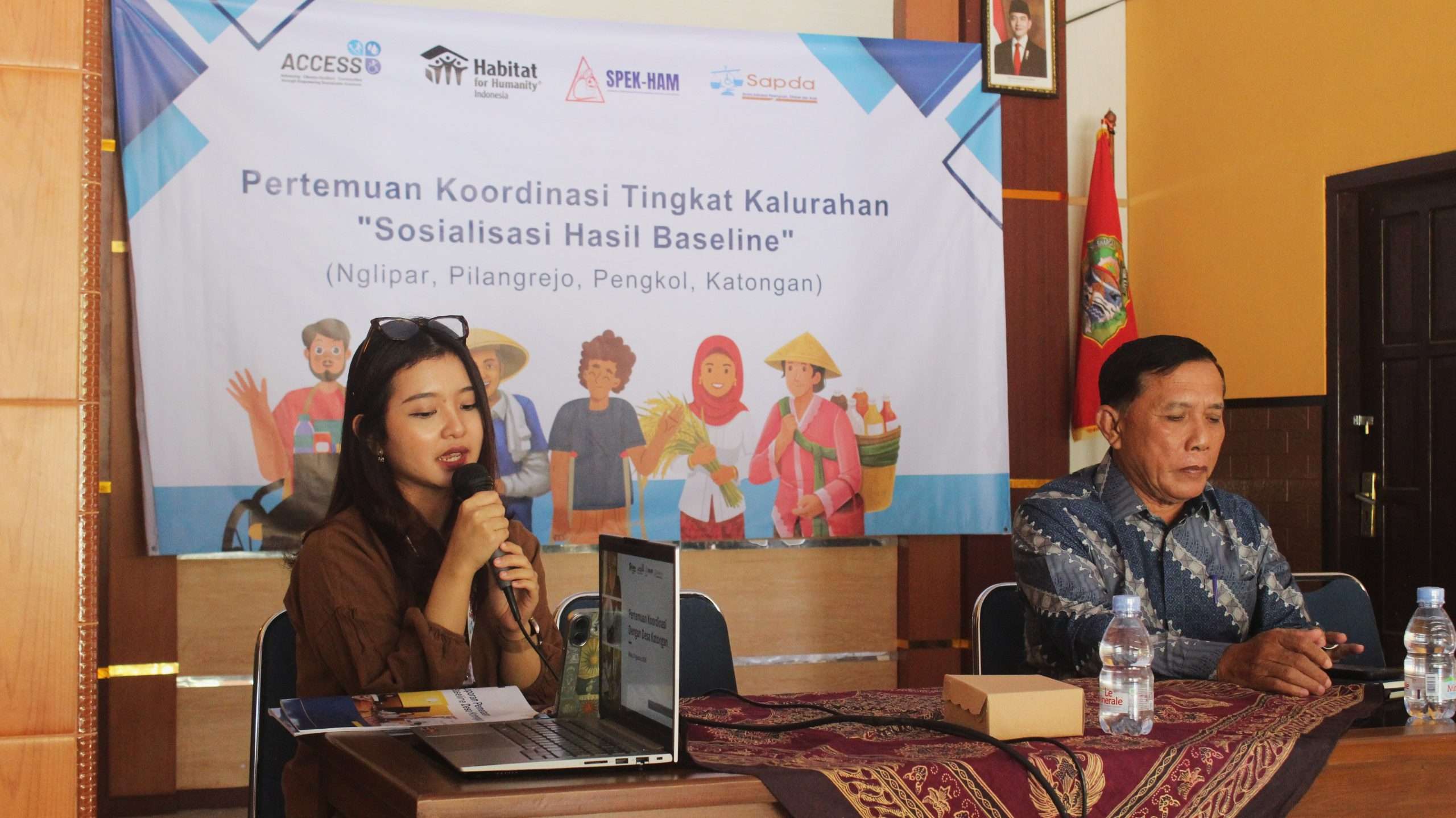 Foto menunjukkan perempuan muda berambut hitam sedang memegang mikrofon dan berbicara dalam kegiatan sosialisasi hasil baseline tingkat kelurahan